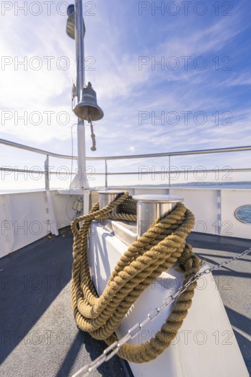 A ship deck with thick ropes and a bell, in front of a clear blue sky at sea, boat trip, Lake Constance, Germany