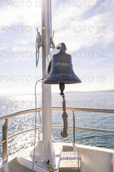 Ship bell on the bow of a boat, shining against the blue sky over calm sea, boat trip, Lake Constance, Germany