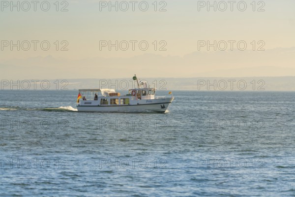 Small white boat with people sailing on a calm lake in sunlight, boat trip, Lake Constance, Germany