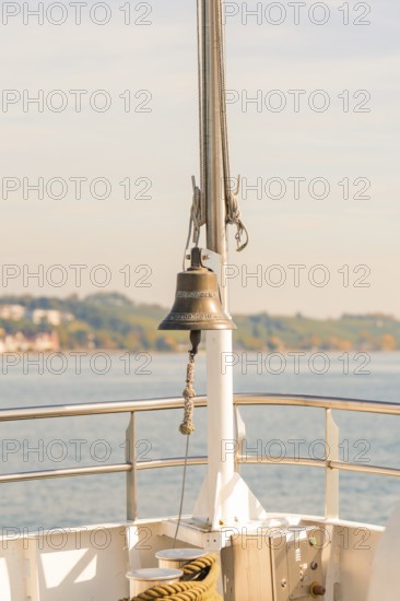 Bell on a ship deck with a view of a sunny coastal landscape, boat trip, Lake Constance, Germany