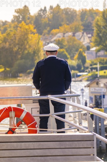 Captain standing at the helm of a boat with an autumn view, boat trip, Lake Constance, Germany