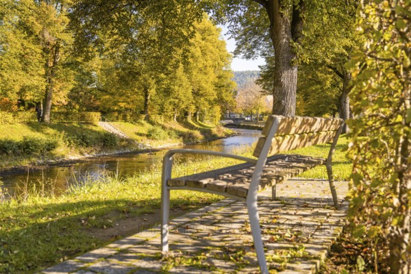 Inviting sitting area in a sunny park with a view of a river and autumn trees, Nagold, Black Forest, Germany