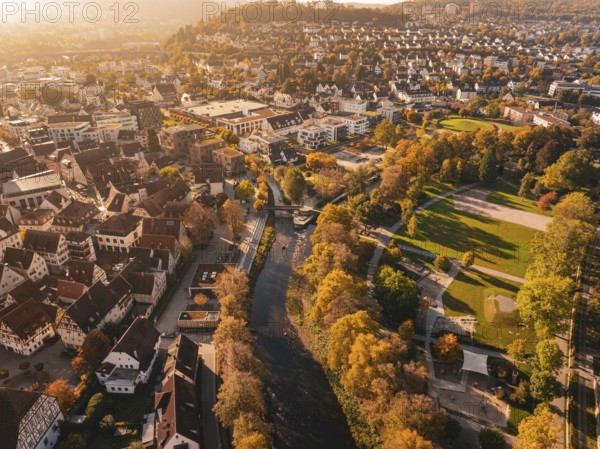 An autumnal view of the city with a river and lots of colorful trees illuminated by the sun, Nagold, Black Forest, Germany