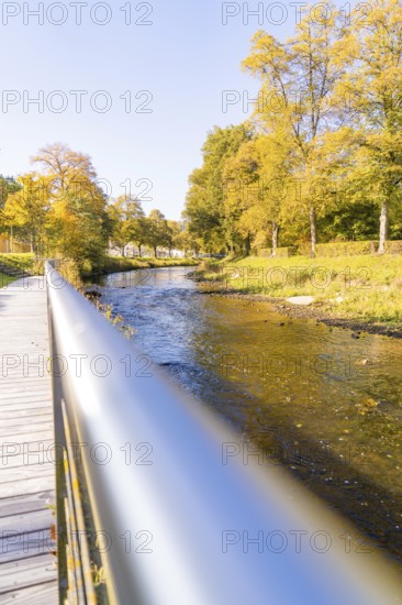 A river flows under a bridge, surrounded by autumn-colored trees on a sunny day, Nagold, Black Forest, Germany
