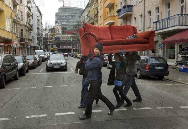 DEU Berlin Young people carry a sofa across Fuldastraße in Berlin Neukölln. The former problem district has been changing for some time due to the influx of students and young creative people from home and abroad. Germany Berlin A Group of New Berlin Citizens Carry a Red Sofa Across the Street