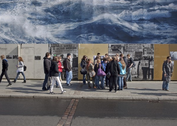 DEU Berlin A giant poster with waves advertising a Norwegian natural gas provider is hanging at Checkpoint Charlie. Germany Berlin A Banner of a Giant Waves Hangs on Checkpoint Charlie as Tourist Visit the Sight