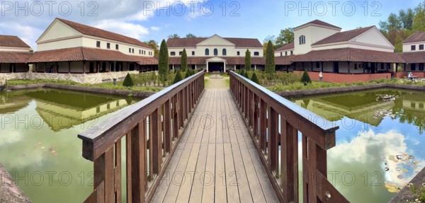 View from site of archaeological open-air museum across small wooden bridge across ornamental pond to reconstructed main building Manor House of Archaeological Park Römische Villa Borg, Perl, Saarland, Germany