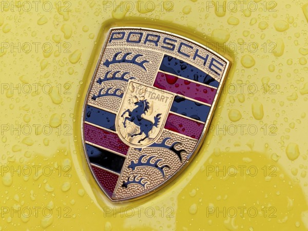 Colored Porsche crest on yellow sports car bonnet with sparkling raindrops, international