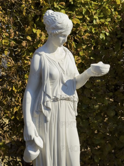 Statue of in Greek mythology goddess of youth Hebe Roman goddess Iuventas of male youth holding a sacrificial bowl in the garden of the open-air museum archaeological park Römische Villa Borg, Perl, Saarland, Germany