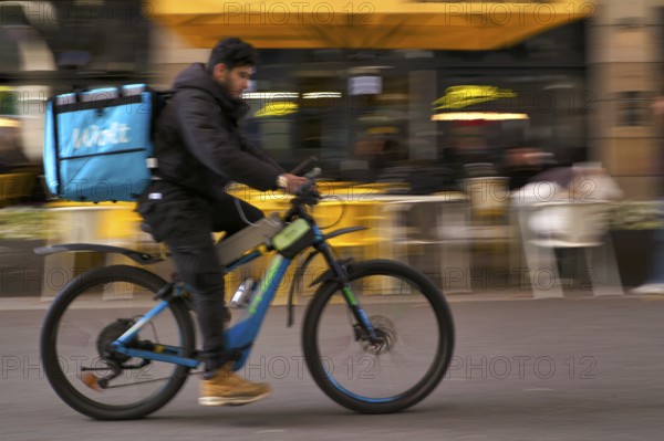 Wolt Enterprises Oy, logo, delivery service, courier service, bicycle courier, courier driver rides with thermal backpack, e-bike, mobile phone, smartphone, movement effect, speed, blurred, Stuttgart, Baden-Württemberg, Germany