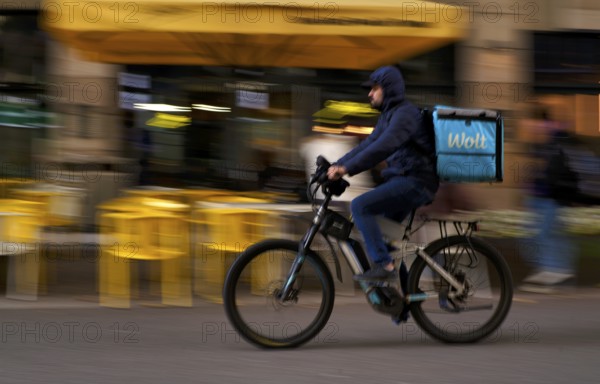 Wolt Enterprises Oy, logo, delivery service, courier service, bicycle courier, courier driver rides with thermal backpack, e-bike, mobile phone, smartphone, movement effect, speed, blurred, Stuttgart, Baden-Württemberg, Germany