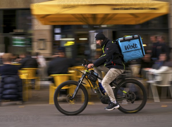 Wolt Enterprises Oy, logo, delivery service, courier service, bicycle courier, courier driver rides with thermal backpack, e-bike, mobile phone, smartphone, movement effect, speed, blurred, Stuttgart, Baden-Württemberg, Germany