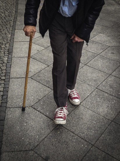 DEU Germany Germany Berlin Old man with a crutch walking through the German capital wearing Converse shoes