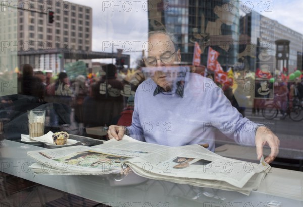 Germany Berlin Anti-nuclear power demonstration in Berlin Mitte. Visitor reads newspapers in a cafe, in front of which a demonstration against nuclear energy is taking place. Germany Berlin protest rally against nuclear power plants. Visitor reads a newspaper