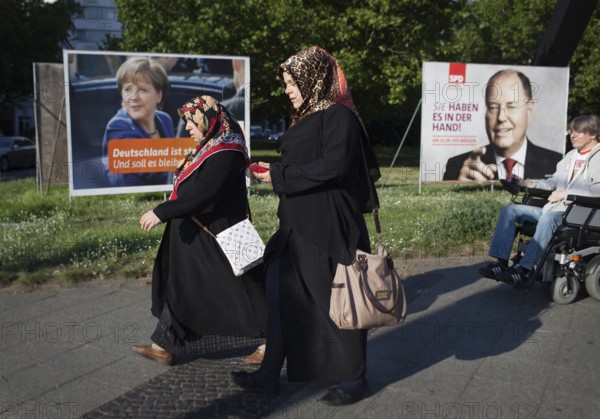 DEU Germany Germany Berlin Two Muslim woman and a man in a wheelchair pass the election posters of Angela Merkel CDU and Peer Steinbrück SPD