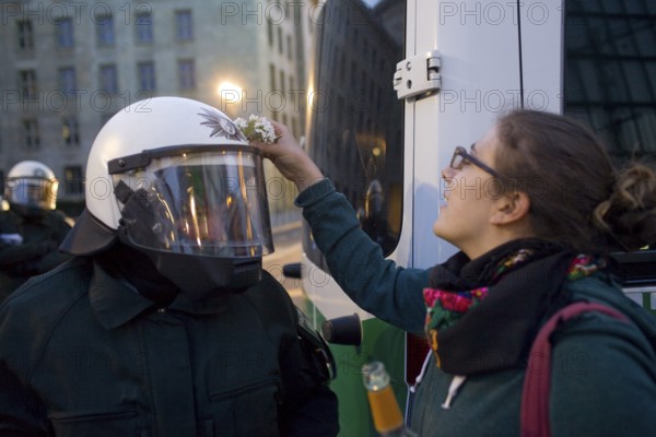 GERMANY Police officers on Leipziger Straße in front of the Ministry of Finance during the May 1 rally. Demonstrator tries to fix an elderberry bush to a policewoman's helmet. Germany Berlin Police in front of the Ministry of Finances during the May Day Protest. Demonstrator Tries to Fix a Flower on a Police Helmet