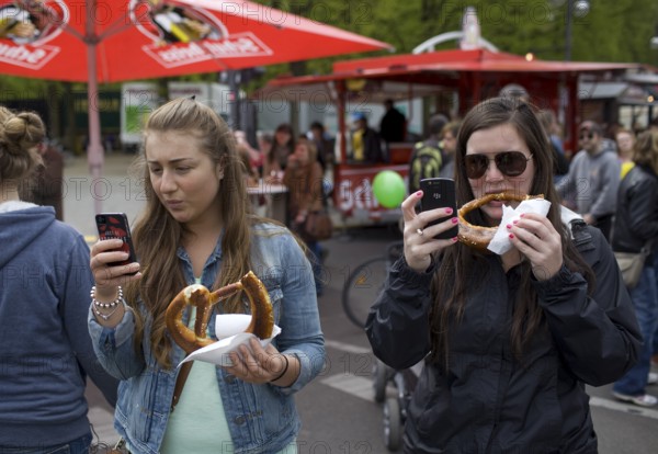 GERMANY Young woman are filming a rally with their mobile phones while eating pretzels. Germany Berlin Young woman shooting with their mobile phones as they are eating pretzels during the May Day protest