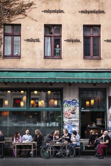 DEU Germany Germany Berlin Guests in front of Bateau Ivre on Oranienstraße in Kreuzberg. A toddler looks out the window of an apartment above