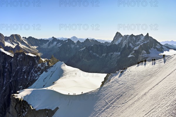 Mountaineers climb over a snow-covered ridge, behind Grandes Jorasses, Aiguille du Midi mountain station, Chamonix-Mont-Blanc, Haute-Savoie, France
