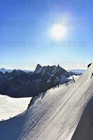 Mountaineers climb over a snow-covered ridge, behind Grandes Jorasses, Aiguille du Midi mountain station, Chamonix-Mont-Blanc, Haute-Savoie, France