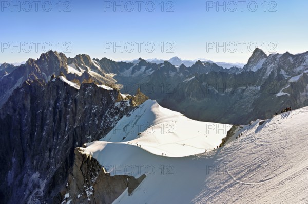 Mountaineers climb over a snow-covered ridge, behind Aiguille Verte, Les Droites, Les Courtes, Grandes Jorasses, Aiguille du Midi mountain station, Chamonix-Mont-Blanc, Haute-Savoie, France
