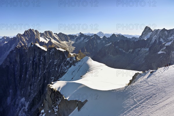 Mountaineers climb over a snow-covered ridge, behind Aiguille Verte, Les Droites, Les Courtes, Grandes Jorasses, Aiguille du Midi mountain station, Chamonix-Mont-Blanc, Haute-Savoie, France