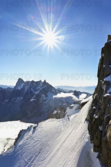 Mountaineers climb over a snow-covered ridge, behind Grandes Jorasses, Aiguille du Midi mountain station, Chamonix-Mont-Blanc, Haute-Savoie, France
