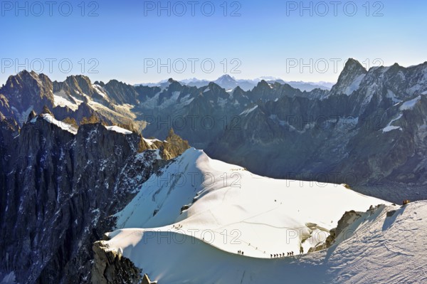 Mountaineers climb over a snow-covered ridge, behind Aiguille Verte, Les Droites, Les Courtes, Grandes Jorasses, Aiguille du Midi mountain station, Chamonix-Mont-Blanc, Haute-Savoie, France