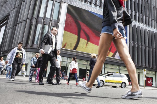 DEU Germany Germany Berlin Passers-by in front of a projection screen on Kurfürstendamm, on which a commercial featuring a large German flag is being broadcast