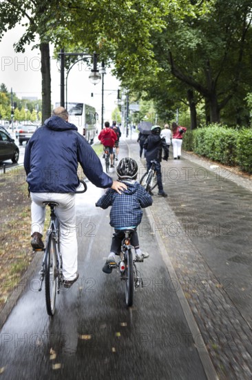 DEU Germany Germany Berlin Cyclists have their arms on a child's back as they cycle towards the Brandenburg Gate