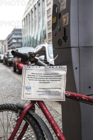 DEU Germany Germany Berlin Notification to the public order office of an orphaned bicycle chained next to a parking ticket machine