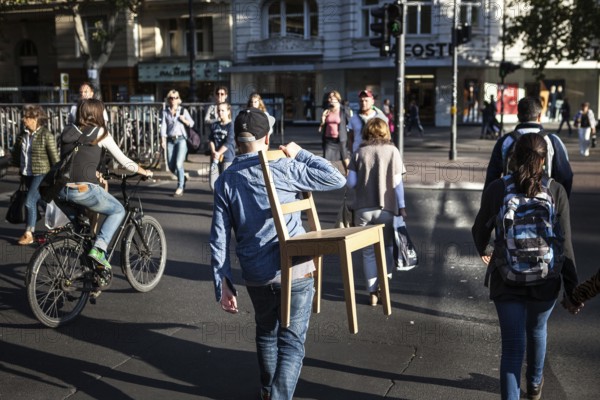 DEU Germany Germany Berlin Man with a chair over his shoulder crosses a pedestrian traffic light on Kudamm