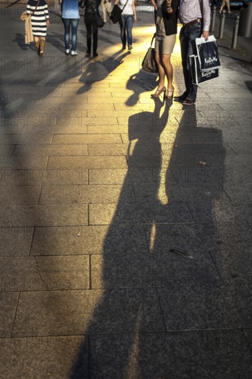 DEU Germany Germany Berlin Passers-by cast their shadow on Berlin's popular shopping street, Tauentzien. The gold of a glass façade is reflected on the sidewalk