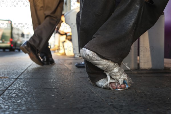 DEU Germany Germany Berlin Homeless person with plastic bag and feet connected to plastic at a bus stop on Potsdamer Platz
