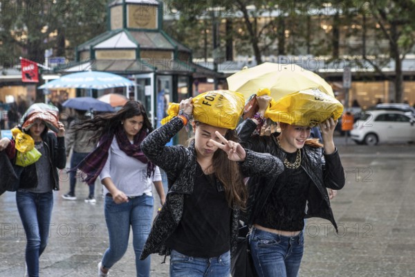 DEU Germany Germany Berlin Young woman walk through the rain, their shopping bags as protection over their heads