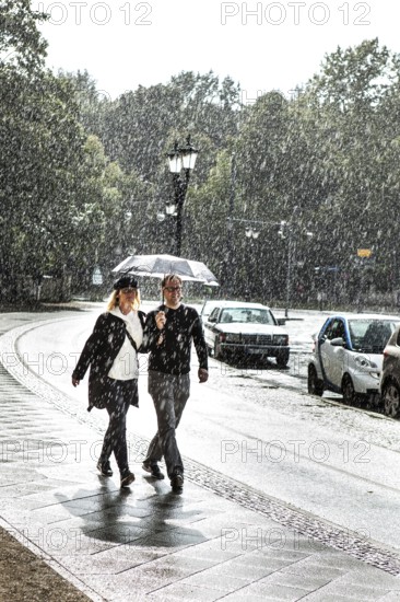 DEU Germany Germany Berlin A couple walking with an umbrella through a summer rain shower at the Victory Column