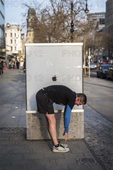 DEU Germany Germany Berlin A jogger does gymnastics in front of an Apple shop display case on Kudamm