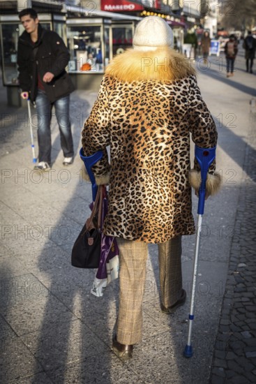 DEU Germany Germany Berlin A woman wears a leopard cloak while using crutches on the Kudamm to pass a man with a crutch