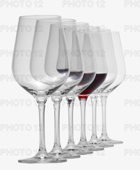 Some wine glasses standing consecutive in a row in white back, one partly filled with red wine