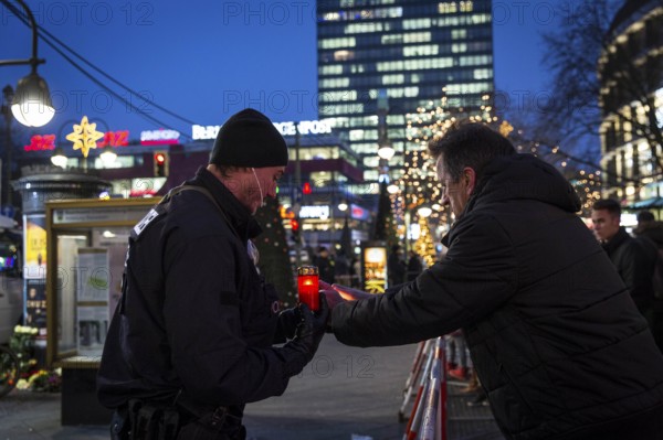 DEU Germany Germany Berlin The second day after the attack on the Christmas market at the Gedächniskirche. A policeman takes a candle from a passer-by to place it at a place of mourning