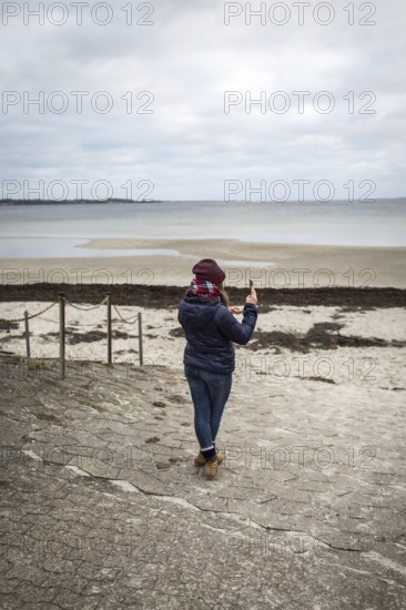 DEU Germany Germany Flensburg A woman takes a photo with her mobile phone on the beach at Holnis