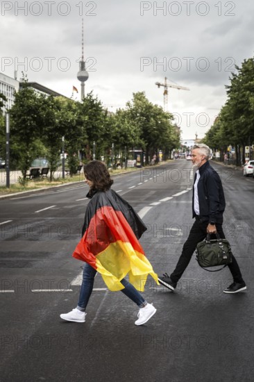 DEU Germany Germany Berlin Tourist with rain capes in the colours of Germany crosses a pedestrian crossing on the street Unter den Linden