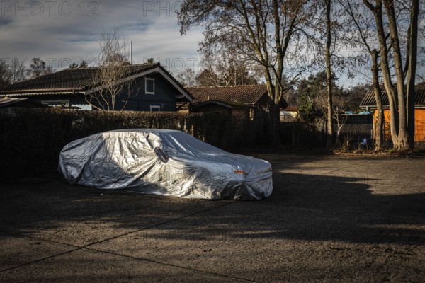 DEU Germany Germany Berlin A car, wrapped in a tarpaulin, is parked in a car park next to an allotment garden in the Grunewald forest