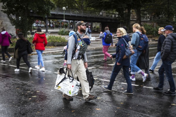 DEU Germany Germany Berlin A father with his two children on his stomach and back walks with shopping bags along the street at Nollendorfplatz