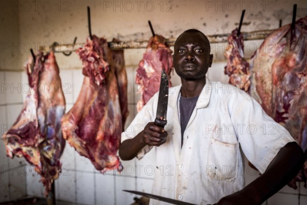 RWA RWANDA Rwanda Kayonza A butcher sharpens his knives in front of pieces of meat. He poses for the photographer ___