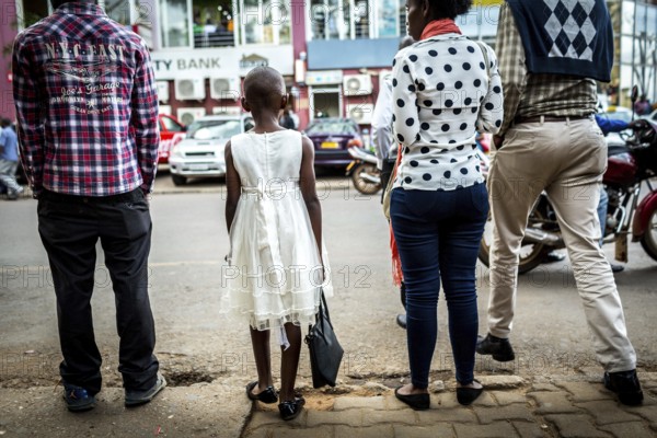 RWA RWANDA RUANDA Kigali A young girl with a white dress and handbag waits with others until she can cross the road