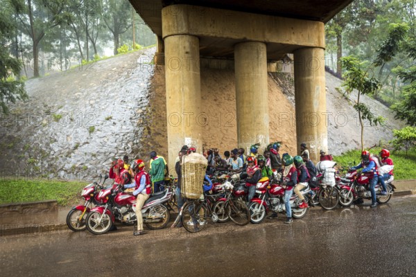 RWA RWANDA RUANDA Kigali Taxi drivers with motorbikes and bicycles wait under a bridge for the end of a rainstorm