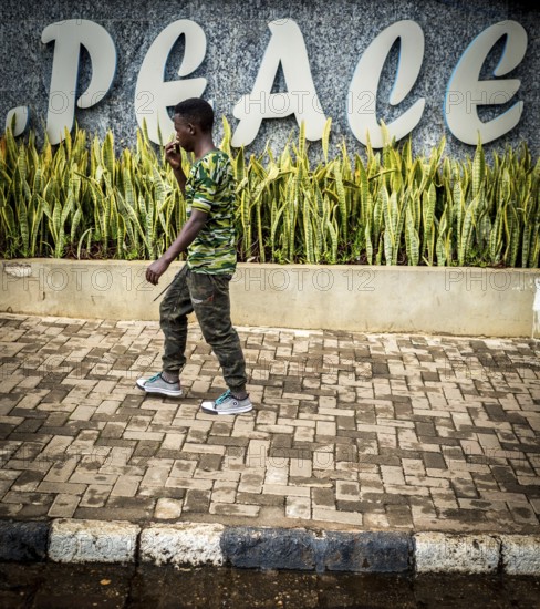 RWA RWANDA RUANDA Kigali A man in camouflage fashion passes a Peace font in the Kiyovu banking district