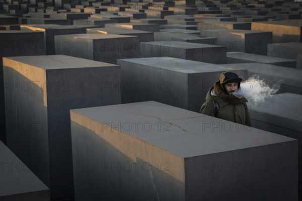 DEU Germany Germany Berlin The Holocaust Memorial as the sun sets. Visitor vaping with an e-cigarette