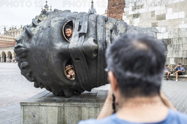 POL Poland Poland Krakow Krakow Asian tourist photographs his children in a sculpture on the Market Square in the Old Town